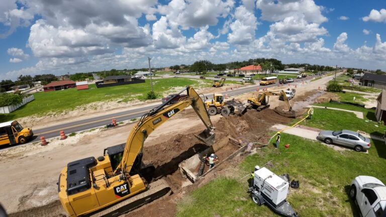 South Florida Bobcat excavator trenching beside a road, drone view
